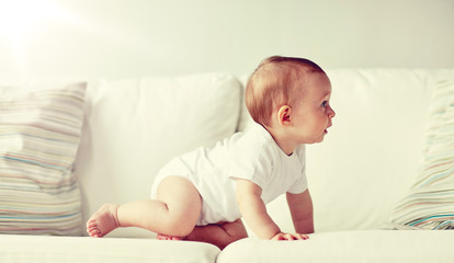 childhood, babyhood and people concept - little baby boy or girl crawling along sofa at home