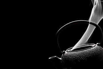 Tea kettle with boiling water. Steaming teapot on black background. Cooking concept.