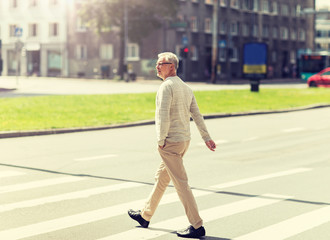 leisure and people concept - senior man walking along summer city crosswalk