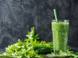 Green smoothie in a glass mug with a straw on the table with ingredients