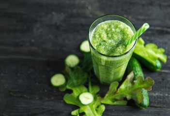 Green smoothie in a glass mug with a straw on the table with ingredients
