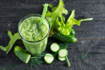 Green smoothie in a glass mug with a straw on the table with ingredients