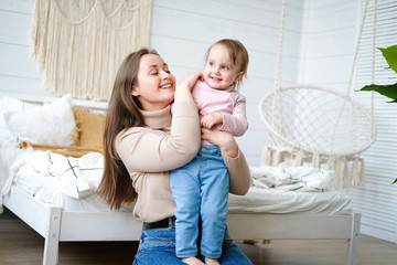 Happy loving family. Young mother are playing with her baby girl in the bedroom. Mom and child are having fun on the bed.