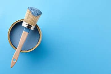 Brush and can of blue paint on blue background, copy space