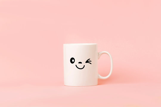 Cup of coffee on pink background with happy smile face on mug
