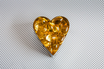 Cod liver oil tablets in a heart shape on a stippled metal background (healthy heart concept)