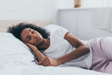 Obraz na płótnie Canvas pretty african american woman in pajamas sleeping on white bedding