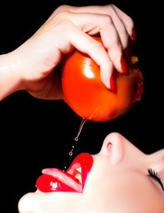 sexy beautiful woman eating juicy ripe tomato isolated on black background