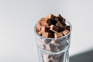 glass full of brown sugar cubes on grey background