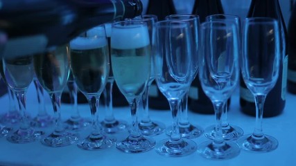 A waiter pours champagne into glasses at a club party. Glasses with champagne on the table are illuminated with different colors of light music. Close-up of glasses