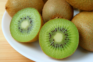 Closeup a plate of whole fruits and cross-sections of fresh ripe kiwi fruits