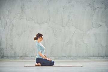 Side view of beautiful Caucasian brunette in sprtswear sitting in Thunderbolt yoga pose.