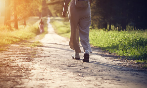 Legs of a girl in light loose pants and white sneakers, which goes in the evening along the path in the Park, illuminated by the rays of the sunset