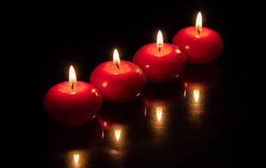 small apple shaped red candles, tealights, burning at night on black. In religious maybe. Isolated on black. 