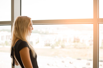 Obraz premium Beautiful blonde girl looks into the large panoramic windows to street.