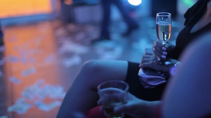 Girl with a glass of white wine in her hand at a party. The girl communicates with the guests at the club. The muted light in the room, lights in different colors.