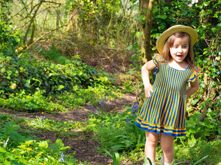 Adorable, smiling little girl in rustic dress and straw hat is playing in spring forest