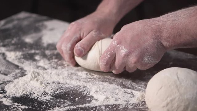Close up view of bakers hands kneading the dough on the table. Manufacturing process, making bread . Slow motion .