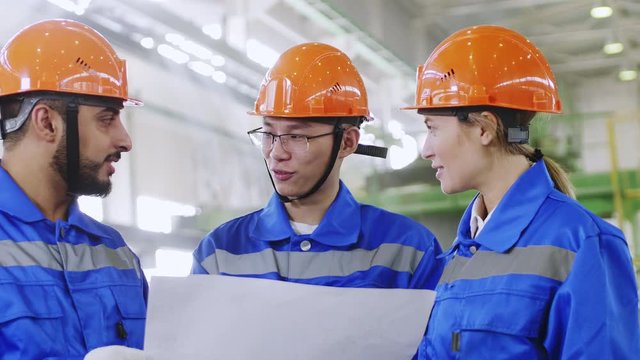 Up-section shot of Asian engineer explaining his international workmates scheme of factory work