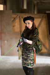 A young woman in an abandoned building with a gun. Laser sight on the machine. Aiming from the machine with a laser. The girl in the black beret, in green camouflage.