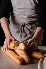 Male hands hold the halves of a baguette and three freshly baked baguettes on the table. Black background.