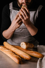 A man with a beard inhales the smell of a freshly baked baguette. Black background.