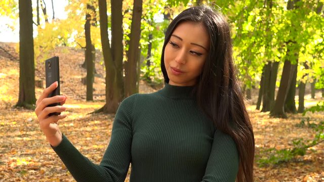 A young Asian woman takes selfies with a smartphone in a park - closeup