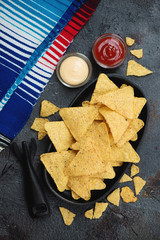 Nachos with dips, flatlay over grey stone background with mexican poncho, studio shot