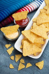 Close-up of nachos chips with dipping sauces, vertical shot over blue stone surface, selective focus