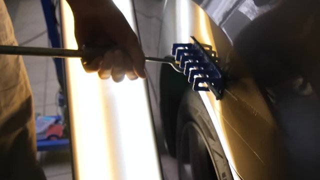 Paintless Dent Repair Removal. Hot glue sticks for removing dents without painting. PDR A man tears blue sticks with a metal tool.