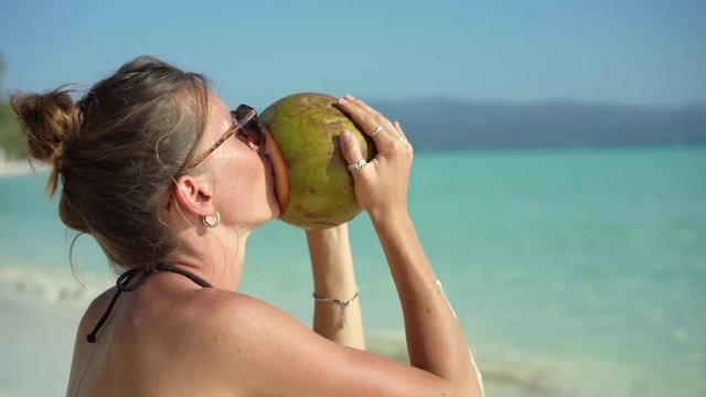 Woman drinking fresh coconut water on beach vacation. Girl relaxing drinking healthy fresh coconut water on tropical sand.