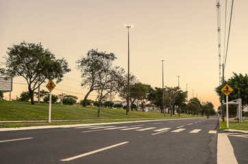 Large avenue with crosswalk. Pedestrians sign.  Avenue with trees around, tall light poles and few traffic at a sunset. Photo at the Afonso Pena avenue, Campo Grande - MS, Brazil.
