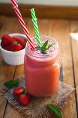 Close-up of strawberry smoothie in a glass jar with fresh mint, on wooden background