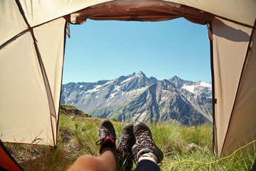 Two pairs of legs in hiking tourist boots at exit of tent