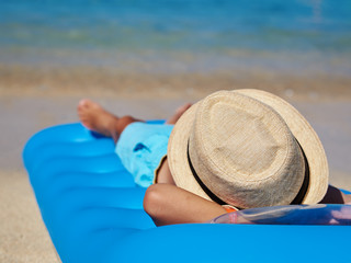 Fototapeta na wymiar European boy in a sun hat enjoying the serenity of ocean laying on the air mattress.