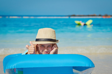 The portrait of smiling European boy in a sun hat in the air mattress at the seashore. He is...
