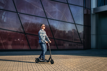 Obraz premium Man riding a electric kick scooter on stone pavement against modern glass wall of building