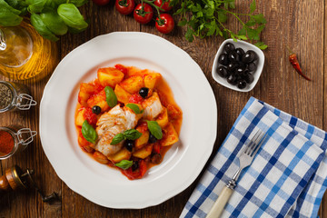 Traditionally prepared cod in Spanish. Served in tomato sauce with boiled potatoes, olivki and basil. Top view.