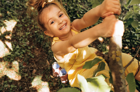 Outdoors image of adorable cute blond little girl playing and smiling broadly at nature background. Happy child swinging on a tree in the summertime in the park. Cheerful kid have fun in the forest.