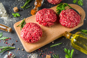 Raw minced meat beef burger cutlets. Cooking meat and burgers background with olive oil. herb, spices, black stone or concrete table, above, copy space