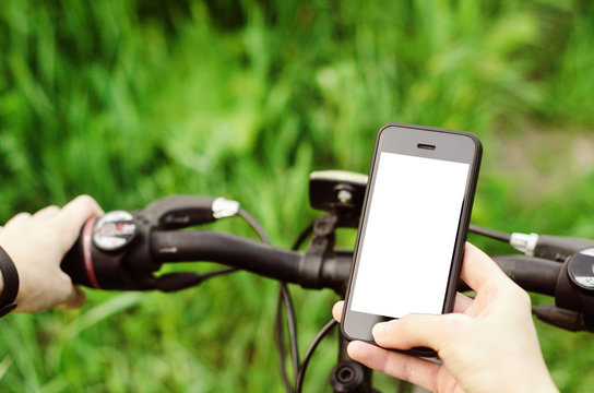 Female hands holding a smartphone while sitting on a mountain bike on a forest road. Concept navigation, summer active sports, technology.