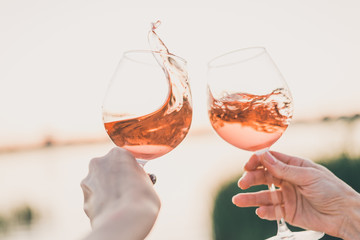 Two glasses of rose wine in hands against the sunset sky.