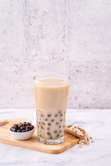Popular Taiwan drink - Bubble milk tea with tapioca pearl ball in drinking glass on marble white table wooden tray background, close up, copy space