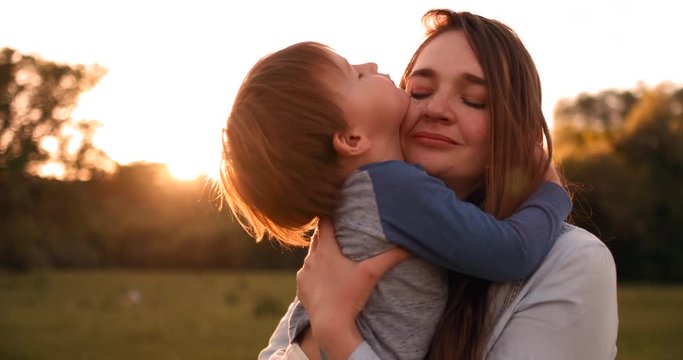 The son kisses his mother sitting at sunset in a field hugging and loving mother. Mother's day.