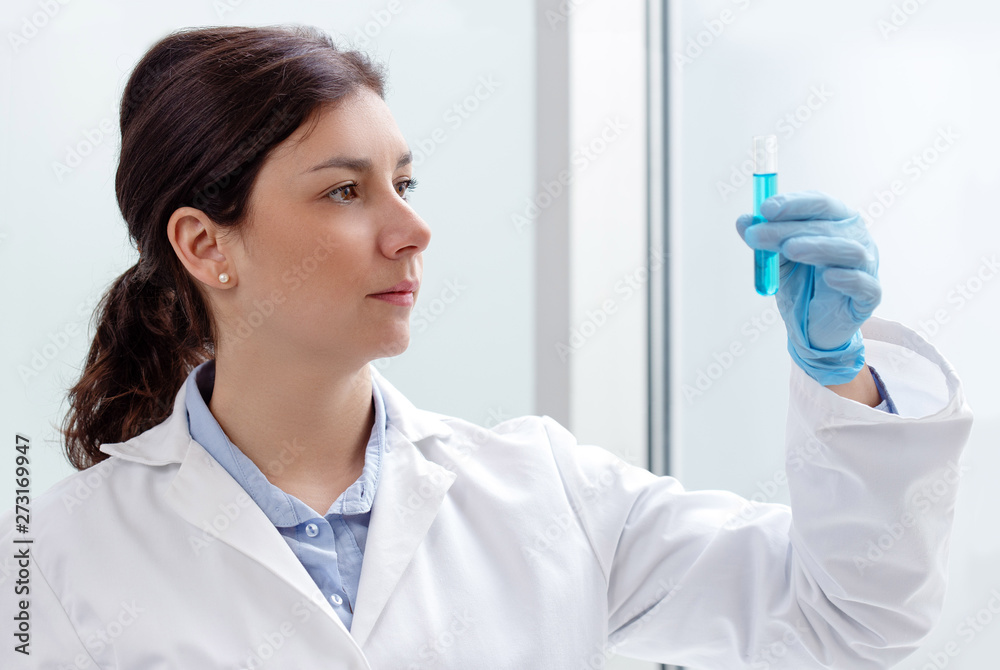 Wall mural young female scientist looking at a test-tube containing blue liquid