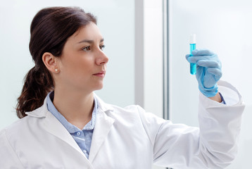 young female scientist looking at a test-tube containing blue liquid - Powered by Adobe