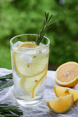 a glass of lemonade with a slice of lemon and rosemary on a white napkin top view