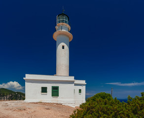 Fototapeta na wymiar Lighthouse building on rocky coast with deep blue sky