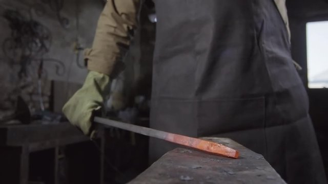 Close up of hot metal billet lying on anvil and hammer striking it