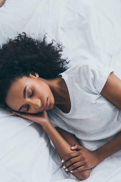beautiful tired african american woman sleeping on white bedding
